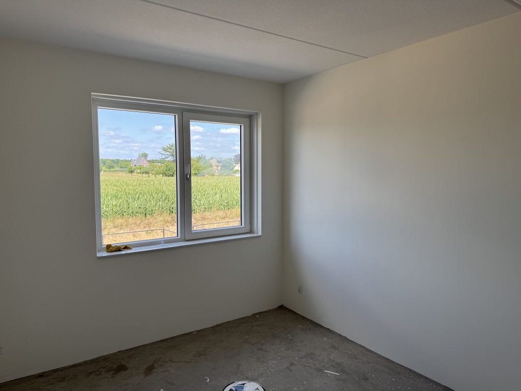 Lege kamer met gladde, lichte wanden en een raam met uitzicht op een veld