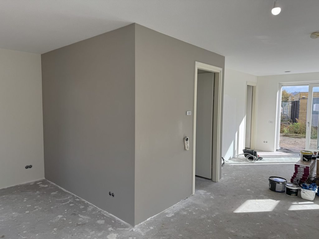 Pas afgewerkte grijze wand in een nieuwbouwwoning met verfemmers op de vloer